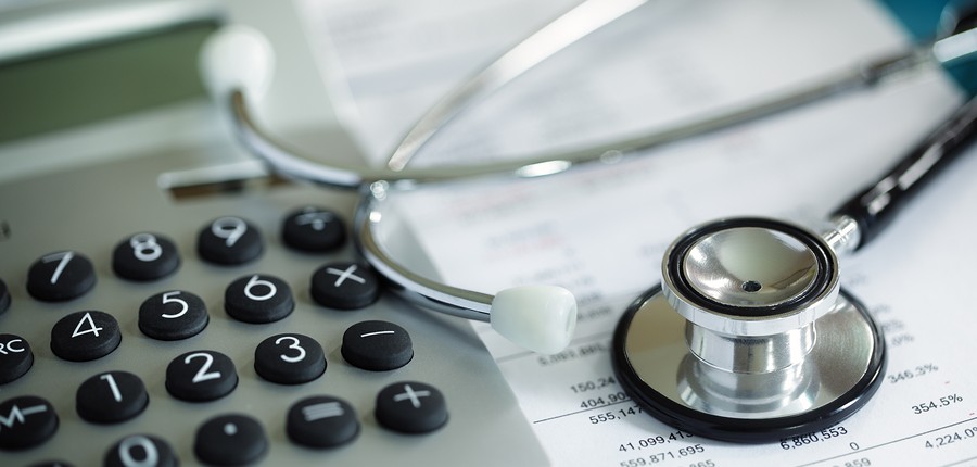 Closeup image of stethoscope with calculator and financial documents.