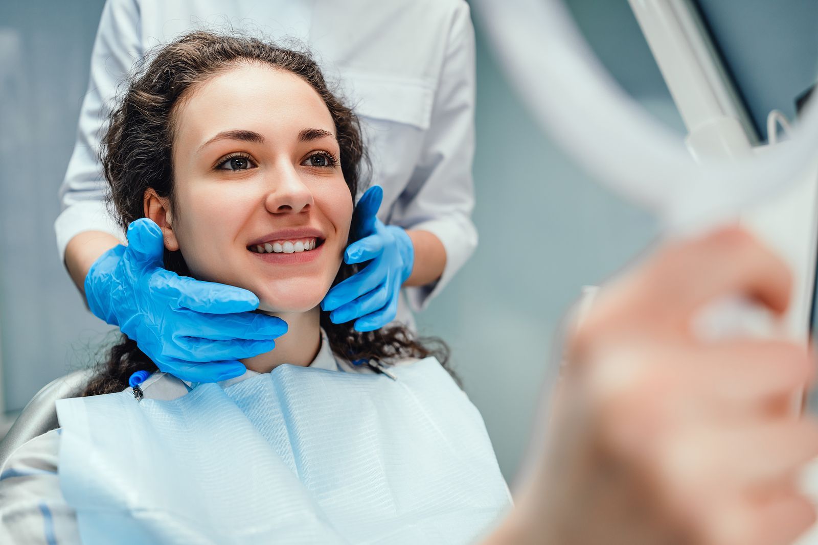 Image of a woman smiling and sitting in a dentist chair while holding a mirror.