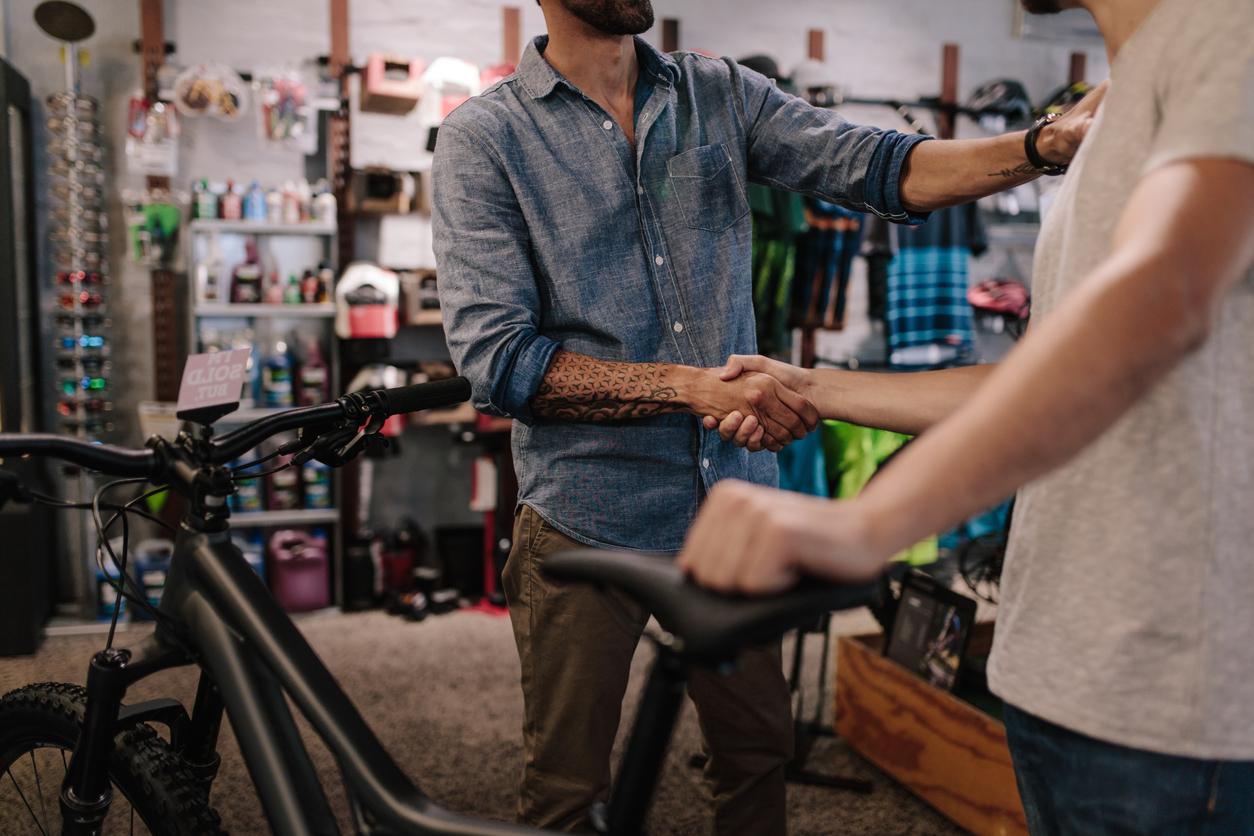Cropped shot of shop owner giving a handshake to a customer after selling a bicycle.