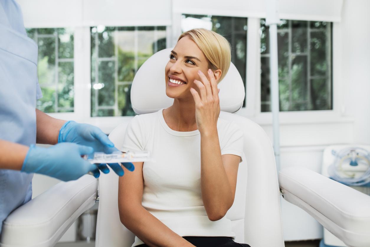 Beautiful and happy blonde woman at beauty medical clinic. She is sitting and talking with female doctor about face esthetics treatment.