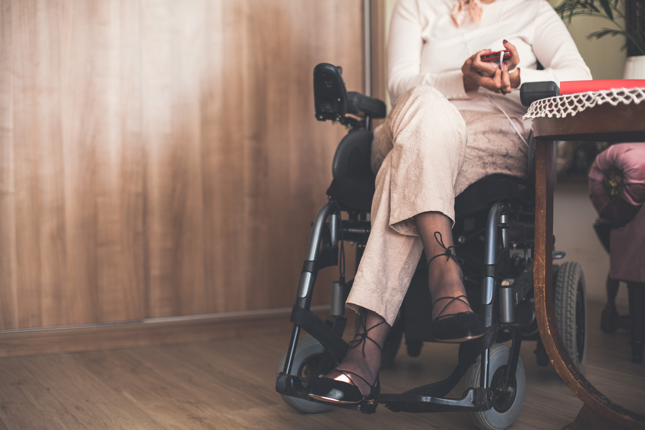 Low section of a woman sitting in wheelchair with legs crossed at knee. She is listening to music using smart phone.